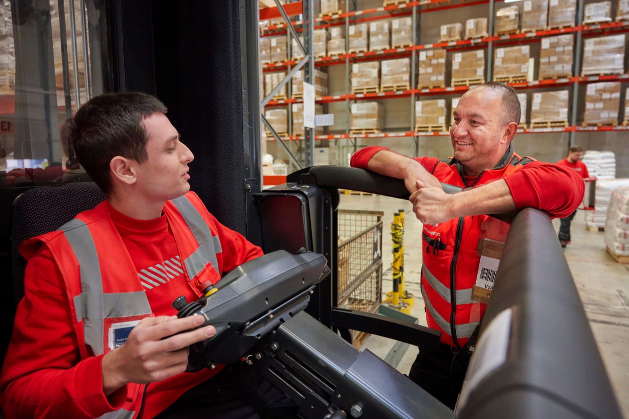 Logistikmitarbeiter in Stapler sitzend im Gespräch in einer Transco Lagerhalle